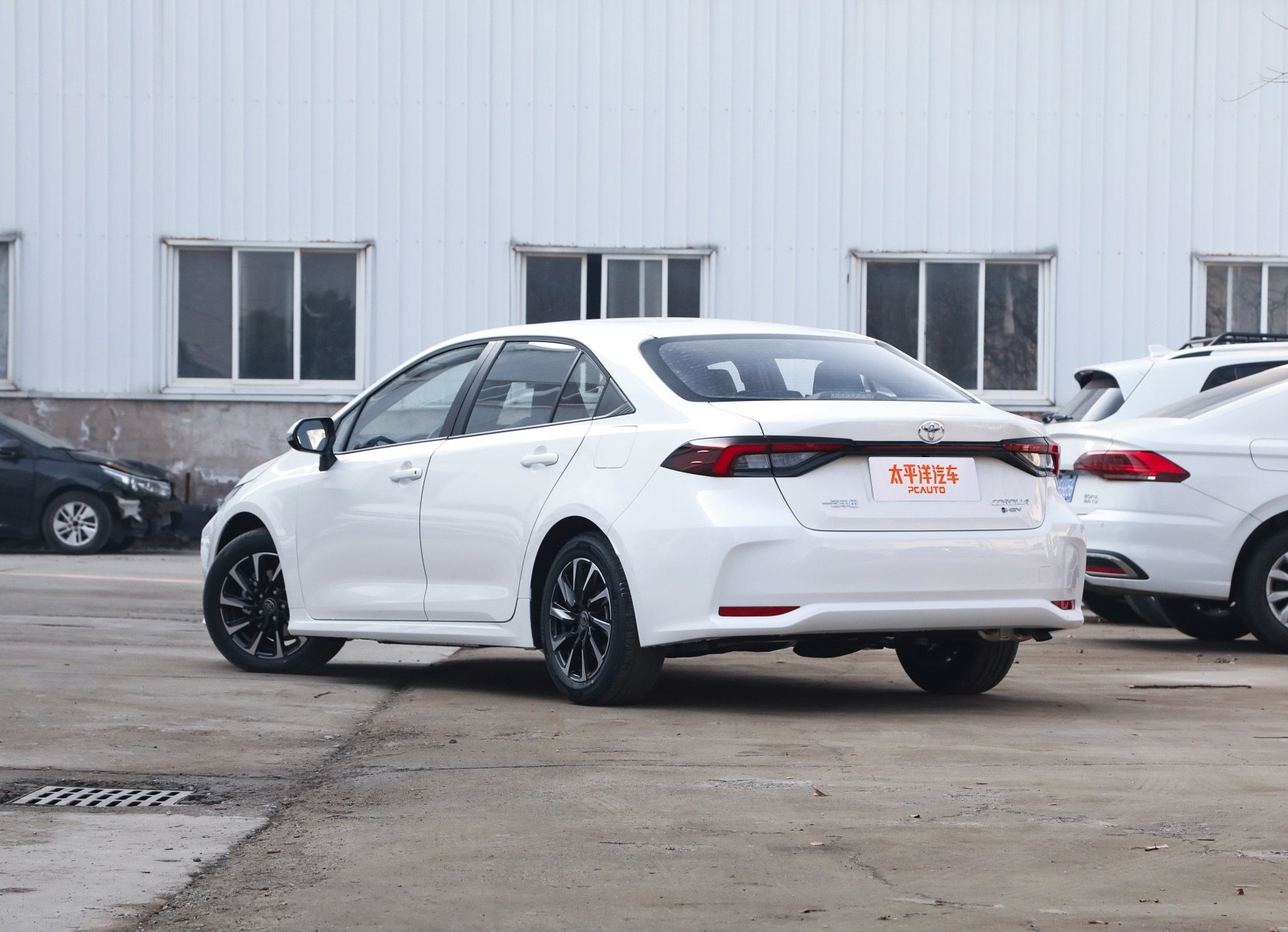 2026 Toyota Corolla white sedan rear side view in parking lot with industrial building background