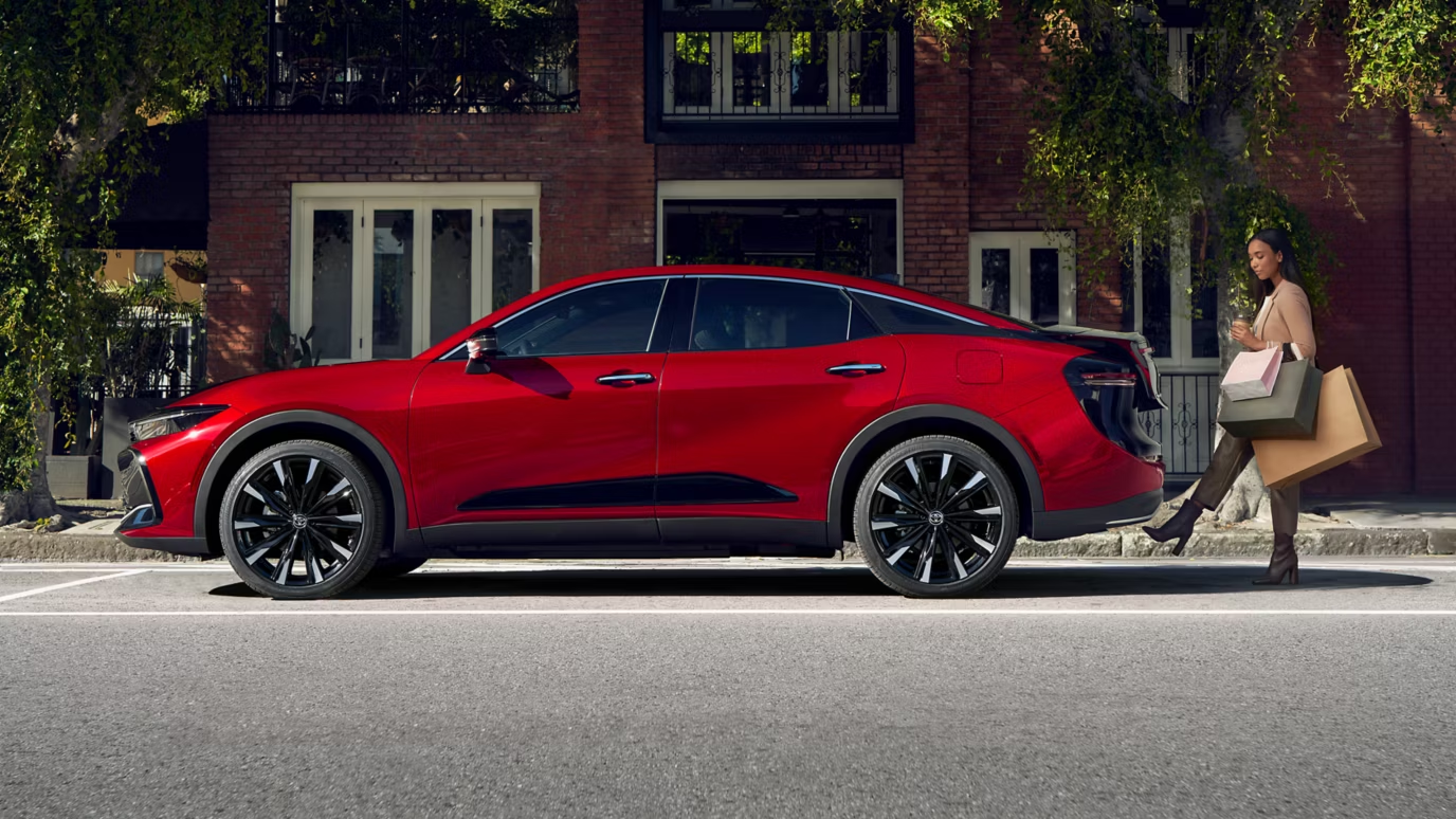 2025 Toyota Crown Crossover สีแดง มุมมองด้านข้างกับผู้หญิงถือถุงช็อปปิ้งบนถนนในเมือง